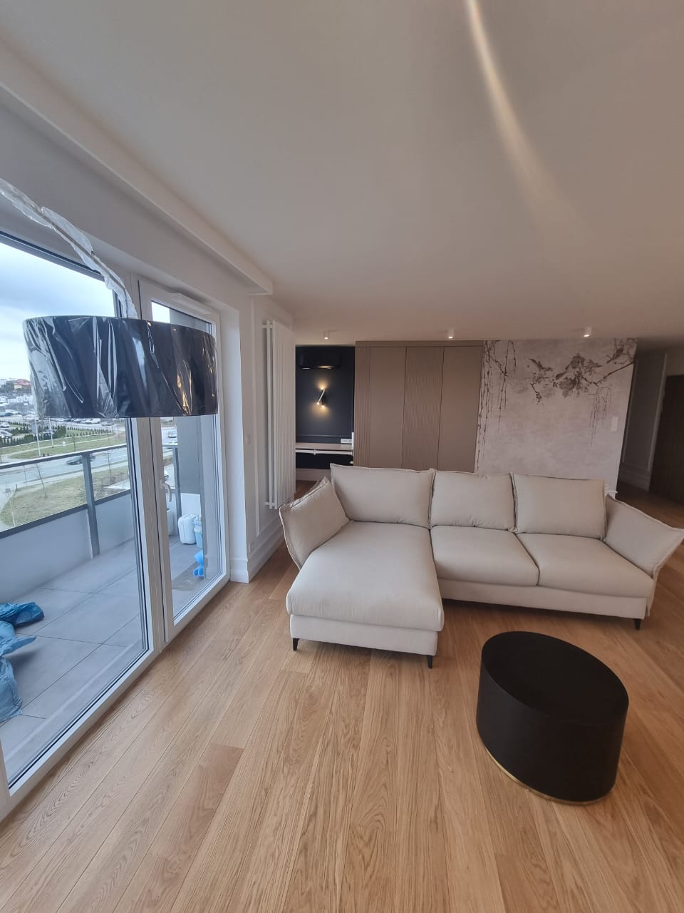 Wykończony salon z jasną sofą, drewnianą podłogą i dużymi oknami